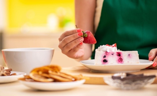 A woman decorating the top of a pie with a strawberry.