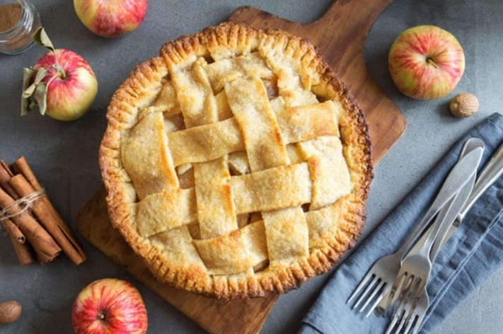 An apple pie displayed with apples on a table.