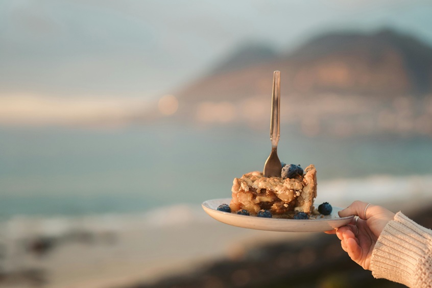 A woman holding a slice of pie looking over a coastal range.