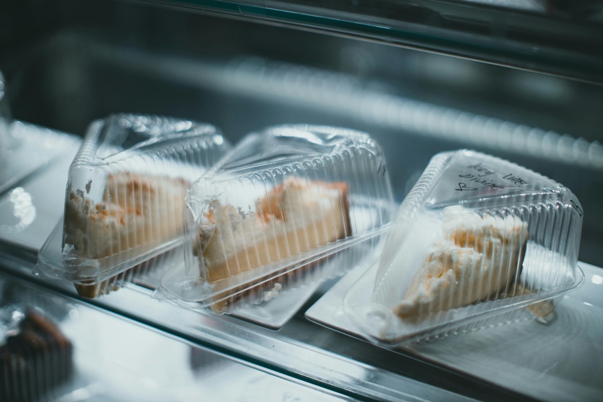 Three pieces of cheesecake displayed in plastic containers on a shop counter